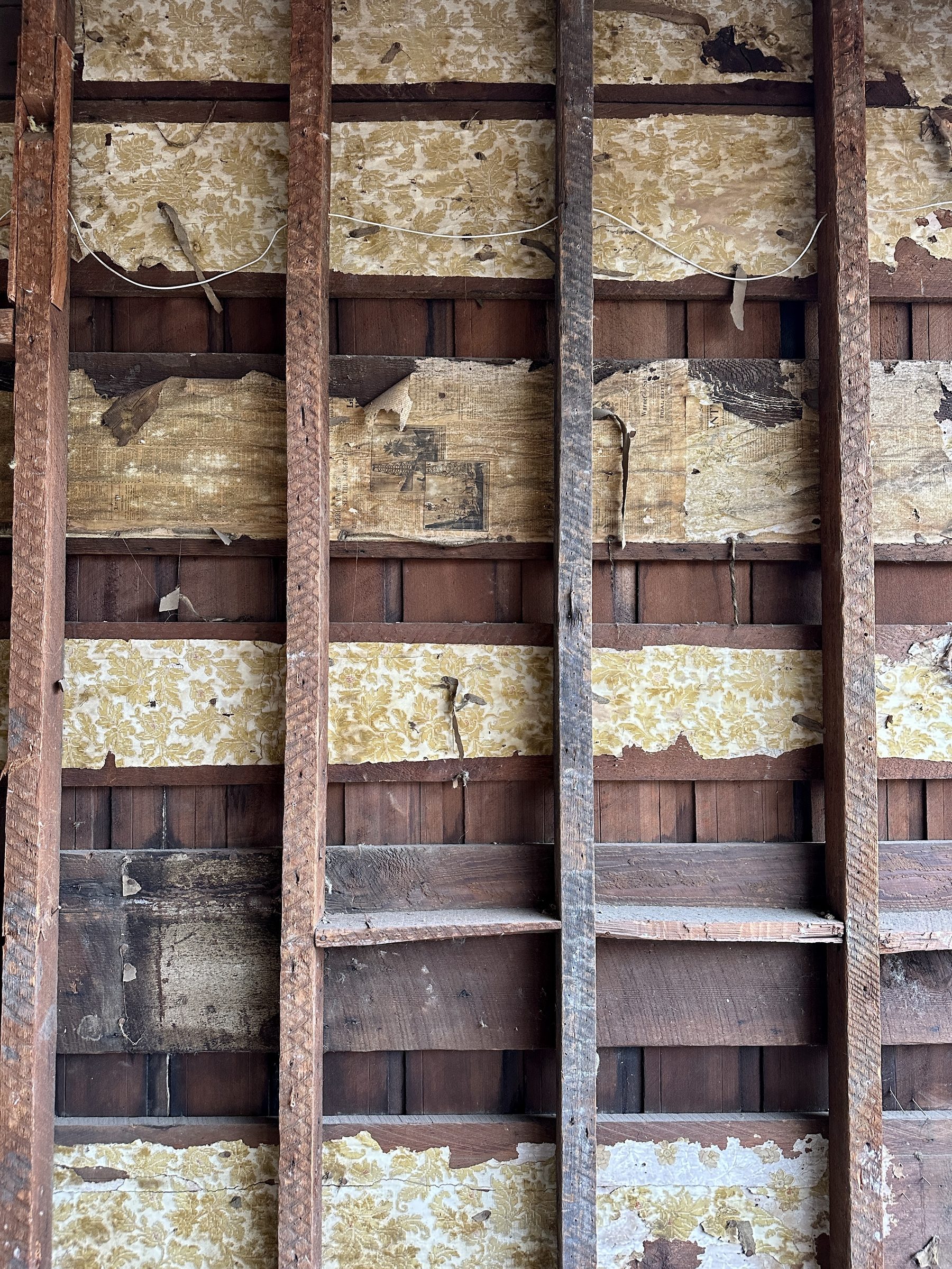 Original wall framing exposed during renovation showing lath, century-old wallpaper, and newspaper